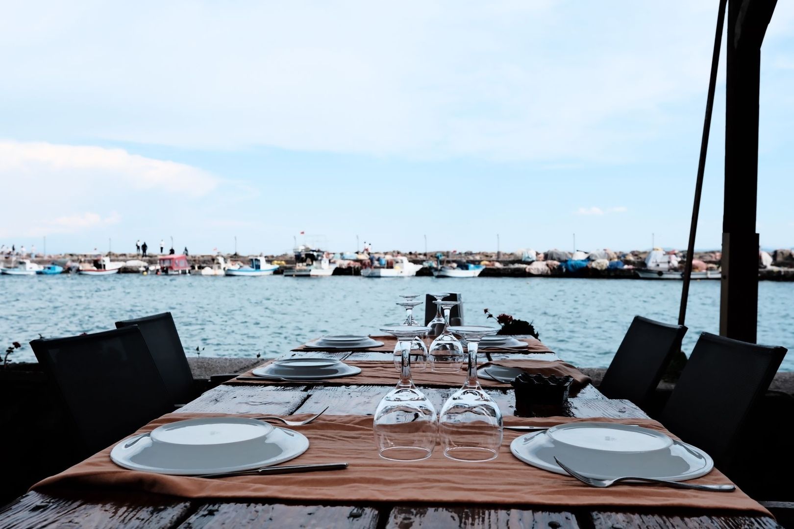 Dukat restaurangbord vid vattnet med båtar och stenpir i bakgrunden