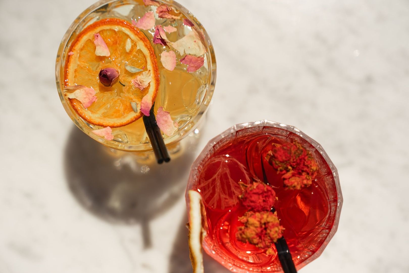 Två färgstarka drycker med citrus, rosenblad och torkade blommor