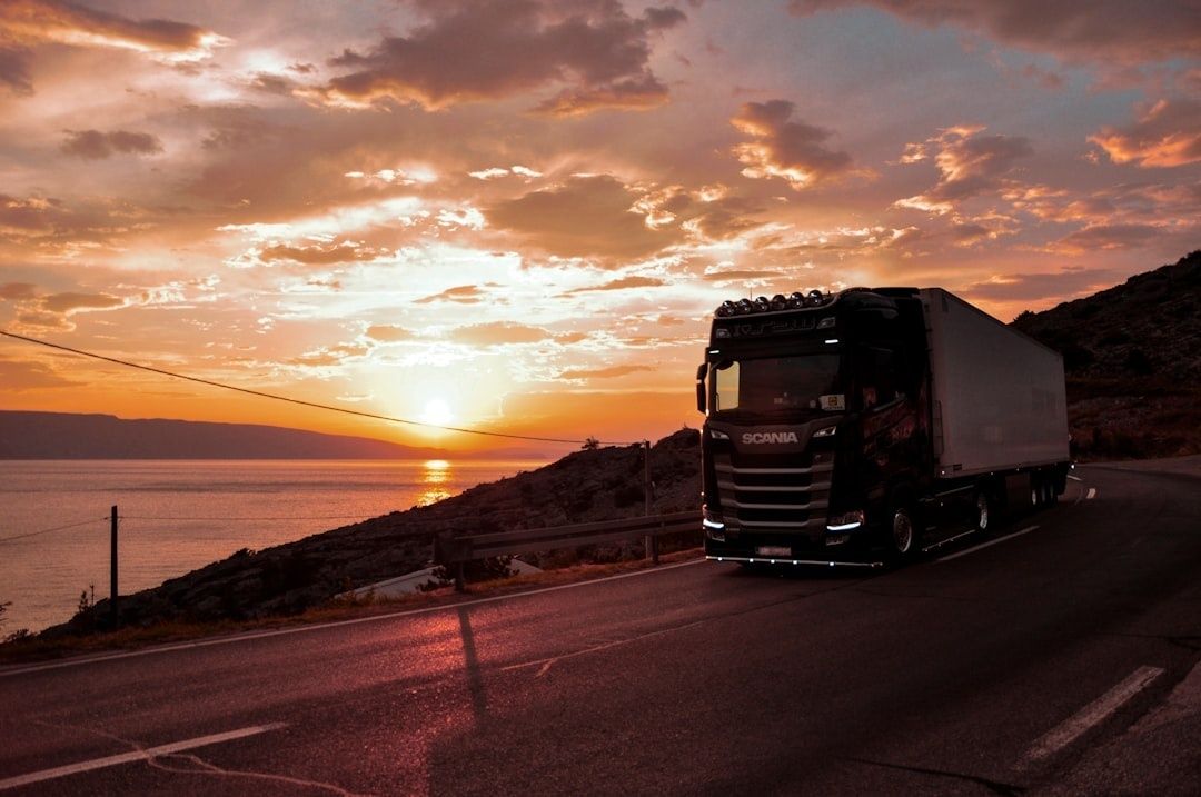 Begagnad Scania-lastbil kör längs en kustväg i kvällsljus